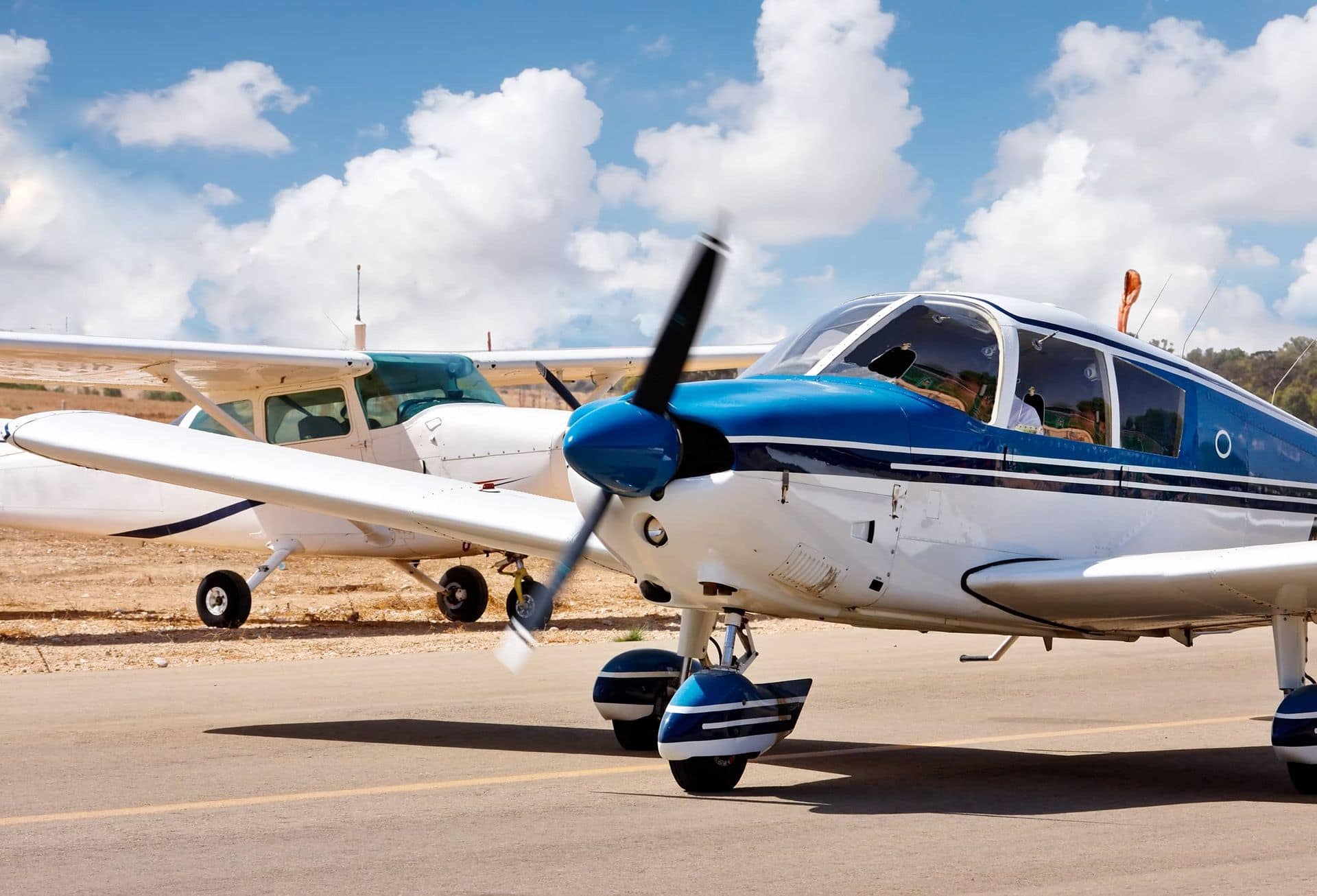 Blue-and-white Piper training aircraft parked on the ramp under towering cumulus clouds