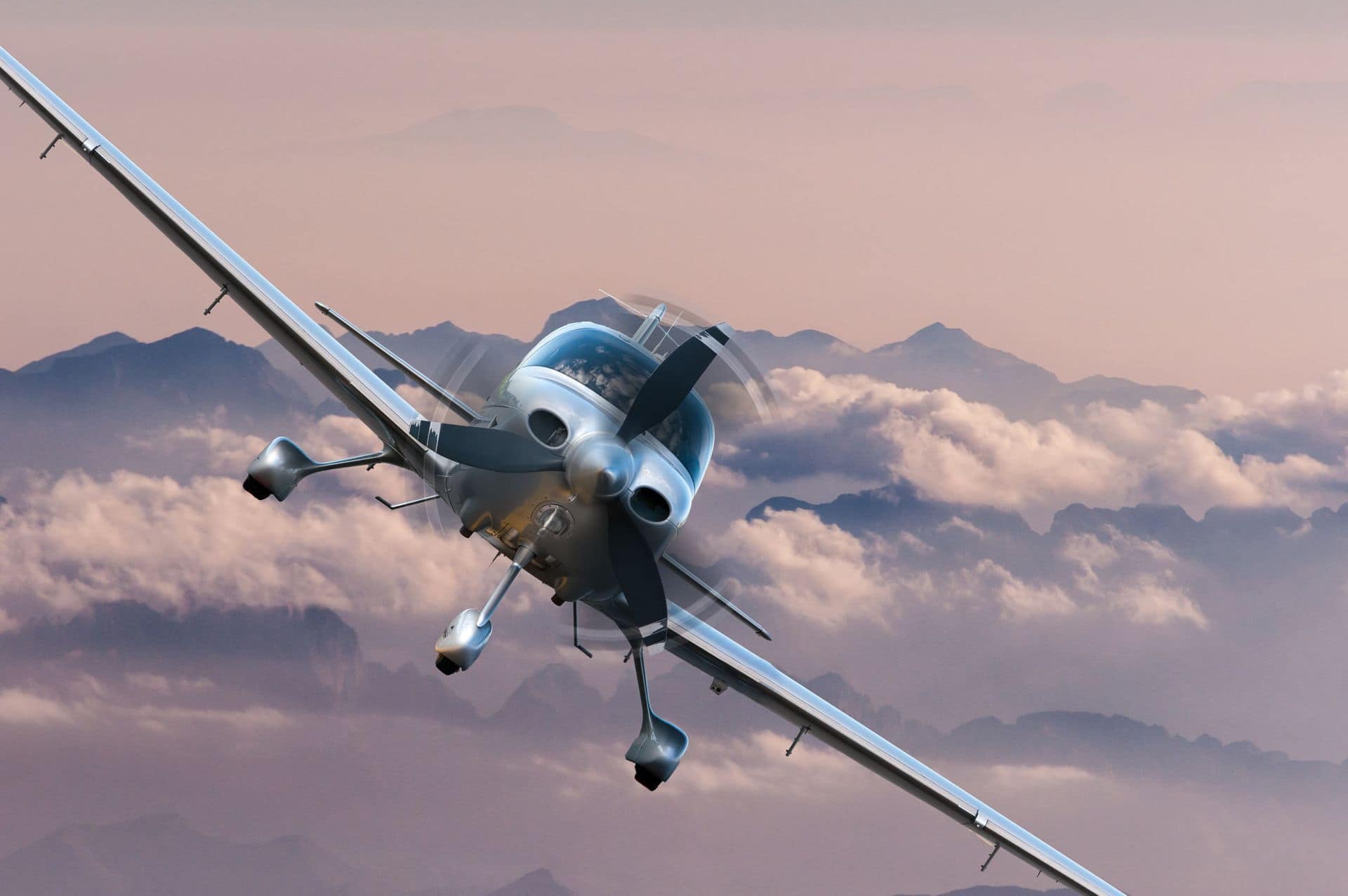 Silver airplane banking above a deck of clouds at dusk